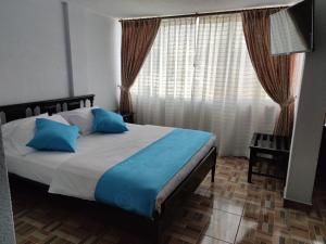 a bedroom with a bed with blue pillows and a window at Val Hotel Santamaria Quito in Quito