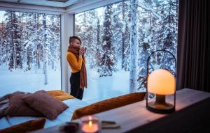a woman taking a picture of a snow covered forest through a window at Arctic Skylight Lodge in Äkäslompolo