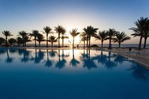a swimming pool with palm trees and the ocean at Sharm Club Beach Resort in Sharm El Sheikh
