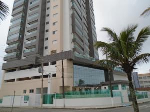 a tall building with a palm tree in front of it at Apartamento em Mongaguá, Frente ao Mar in Mongaguá