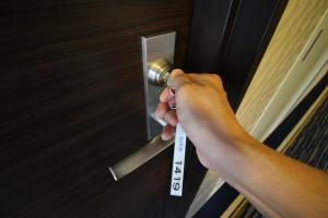 a person holding a door handle with a thermometer at Meitetsu Inn Nagoya Nishiki in Nagoya