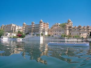 un grand bâtiment avec un bateau bleu dans l'eau dans l'établissement Shiv Niwas Palace by HRH Group of Hotels, à Udaipur