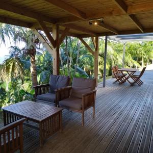 une terrasse couverte en bois avec des chaises et une table. dans l'établissement Lounge des hauts 3 maisons à L'étang-Salé sans vis à vis avec vue panoramique Océan et Montagne, à L'Étang-Salé