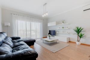 a living room with a black leather couch and a table at Apartamento 7 Mares com Suite in Sagres