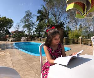 a little girl sitting in a chair reading a book at Pousada Vó Liane in Praia Grande