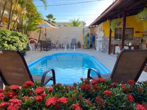 a swimming pool with two chairs and flowers at Pousada Som dos Pássaros in Porto De Galinhas