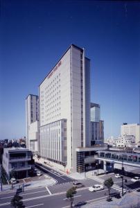 ein hohes weißes Gebäude in einer Stadt mit Autos in der Unterkunft Takaoka Manten Hotel Ekimae in Takaoka