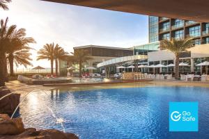 a swimming pool in front of a building with palm trees at Yas Island Rotana Abu Dhabi in Abu Dhabi