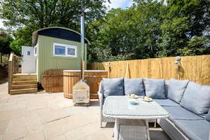 a patio with a couch and a table and a fence at Penlea Retreat Luxury Coastal Shepherds Hut 5 Minute Walk to Pubs and Village in Polperro
