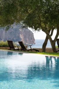 a pool with two chairs and a tree and the ocean at Can Simoneta - Adults Only in Canyamel