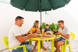 una familia sentada alrededor de una mesa bajo un paraguas en Casa Alegria by CosyCasa Praia Peniche, en Peniche