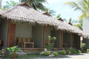 a house with a thatched roof and a palm tree at Bale Karang Cottages in Batukaras