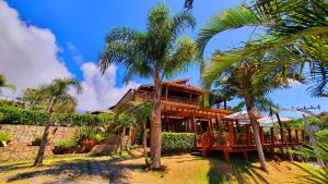 a wooden house with palm trees in front of it at Pousada Paraíso Gaia in Praia do Rosa