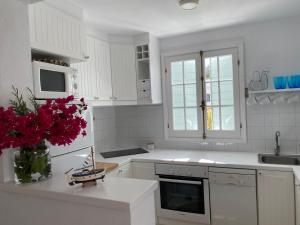 una cocina con armarios blancos y flores rojas en un jarrón en Es Chalet, en Sant Lluis