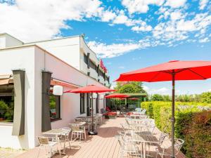 a patio with tables and chairs and red umbrellas at ibis Mulhouse Ile Napoleon in Sausheim