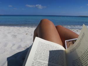 uma mulher deitada na praia a ler um livro em Iocchedda em Porto Ottiolu
