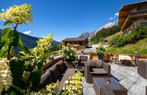 eine Terrasse mit Stühlen, Tischen und Bergen im Hintergrund in der Unterkunft Das Grünholz Aparthotel in Mühlbach am Hochkönig