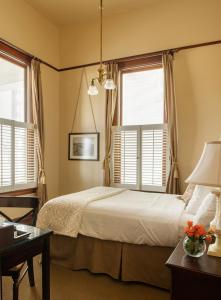 a bedroom with a bed and a desk and two windows at The Sacajawea Hotel in Three Forks