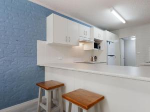 a kitchen with white cabinets and two stools at Bay Parklands 57 ground floor unit with pool tennis court and aircon in Nelson Bay