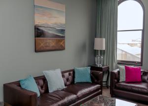 a living room with a brown leather couch and a window at The Old Confectionery in Oamaru