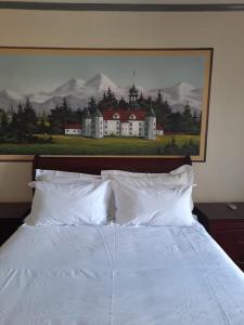 una cama con almohadas blancas y una pintura de una casa en Alpine Inn en George