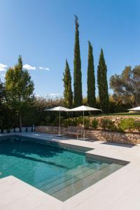 a swimming pool with two umbrellas and trees at Du Côté Des Olivades in Paradou