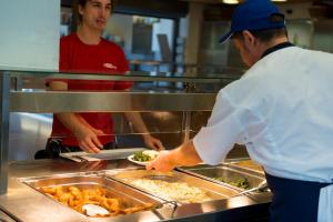 zwei Köche in einer Küche, die Essen in Tabletts zubereiten in der Unterkunft Sport Resort Fiesch, Garni Goneri in Fiesch