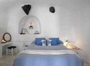 a white bedroom with a blue bed with blue pillows at Altana Heritage Suites in Imerovigli