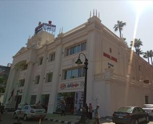 Royal Jewel Al Raml Hotel في الإسكندرية: مبنى ابيض كبير فيه سيارات تقف امامه