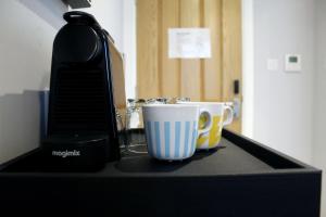 una cafetera y dos tazas de café en una barra en CG Kensington, en Londres