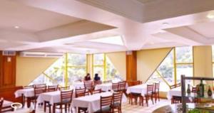 uma sala de jantar com mesas, cadeiras e janelas em Flats termais em condomínio Apart Hotel de águas termais em Gravatal
