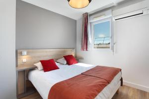 a bedroom with a bed with red pillows and a window at Odalys City Aix en Provence Le Clos de la Chartreuse in Aix-en-Provence