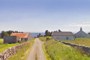 a dirt road in a field with houses and the ocean at Quaint and Quirky Cottage in Port Ellen in Port Ellen