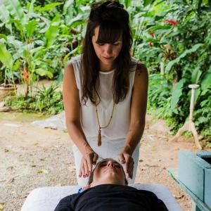 Eine Frau schneidet einem Mann die Haare, während sie auf einem Bett liegt. in der Unterkunft Casa Bacarirá - Floresta com Yoga e Café da Manhã Vegano in Camburi