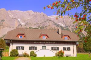 a white building with a brown roof in front of a mountain at Gästehaus Prugger by Schladmingurlaub in Ramsau am Dachstein