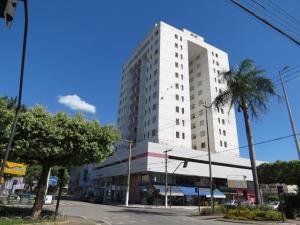 a tall white building on a street with a palm tree at Green Valley Hotel in Timóteo