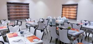 uma sala de jantar com mesas e cadeiras brancas e janelas em Alim Royal Hotel and Suite em Abuja