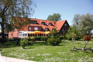 a large red house with a yard with white flowers at Hotel & Restaurant Am Wasser in Breege