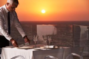 Um homem está a pôr uma mesa num restaurante. em Bellevue On The Beach Suites in Ilha de Rhodes