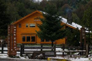 una cabaña de madera en la nieve con un árbol delante en Alto Melimoyu Hotel & Patagonia, en La Junta