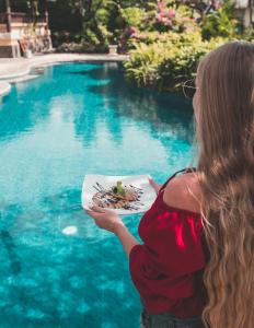 a woman holding a plate of food next to a swimming pool at Santai Hotel in Amed