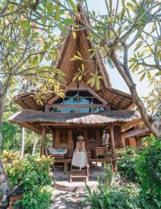 a resort with a thatched roof and a woman sitting in a chair in front at Santai Hotel in Amed