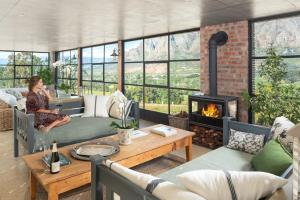 a woman sitting on a couch in a living room with a fireplace at De Zeven in Stellenbosch