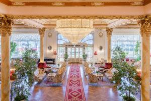 eine große Lobby mit Tischen, Stühlen und einem Kronleuchter in der Unterkunft Hotel Regina Palace in Stresa