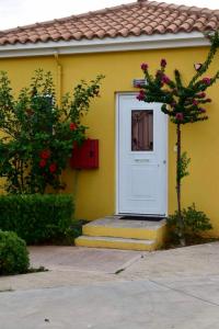 een geel huis met een witte deur en een boom bij Boutique Hotel Ileas Village in Arkoudi