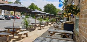 a row of tables and benches with umbrellas on a street at The Queen Catherine Hotel in Osmotherley