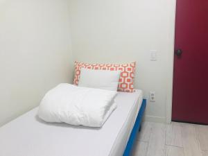a white bed with an orange and white pillow on it at Slow Citi Guest House in Seogwipo