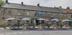 a building with tables and umbrellas in front of it at The Queen Catherine Hotel in Osmotherley