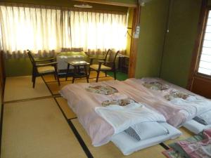 two beds in a room with a table and chairs at Uotoshi Ryokan in Yamanouchi