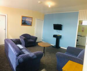 a living room with two blue chairs and a tv at Turn-in Motel in Warrnambool